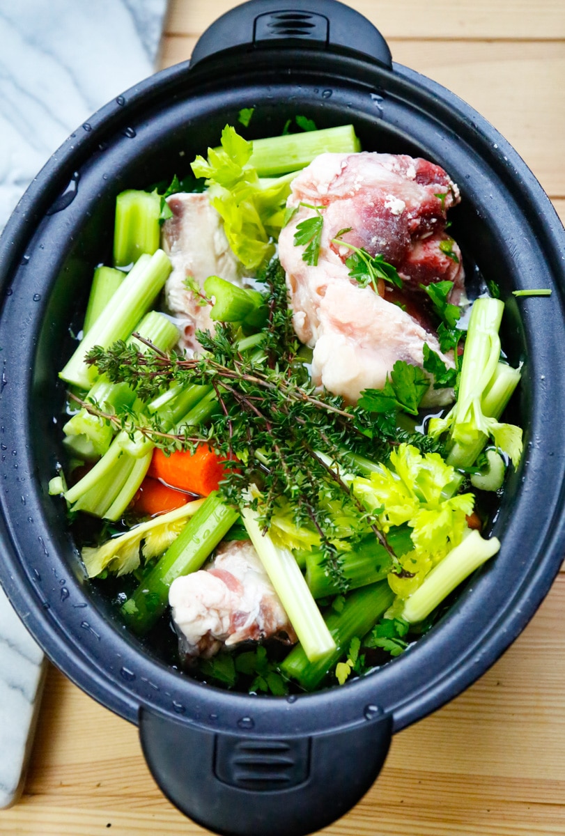 a crockpot filled with beef marrow bones, celery, carrots, and fresh thyme 