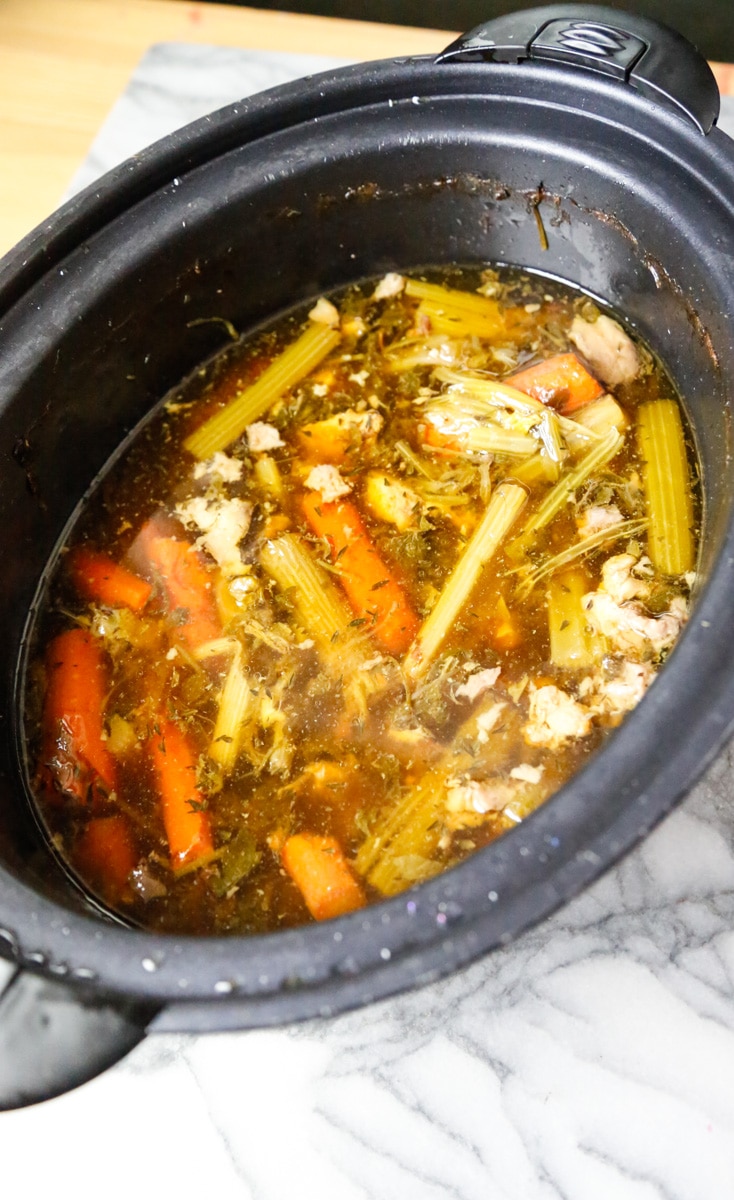 homemade bone broth recipe for dogs in a slow cooker filled with carrots, celery, beef knuckle bones, parsley and thyme 