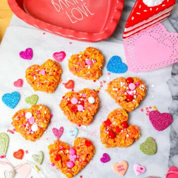crispy cornflake cookies for Valentines day on marble backdrop with heart lights and colored hearts and a heart shaped baking pan that says baking love