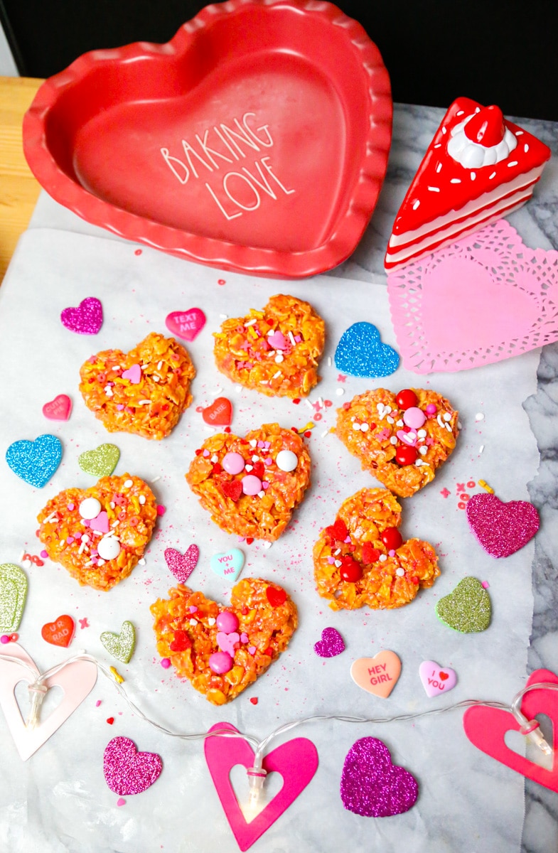 crispy cornflake cookies for Valentines day on marble backdrop with heart lights and colored hearts and a heart shaped baking pan that says baking love 