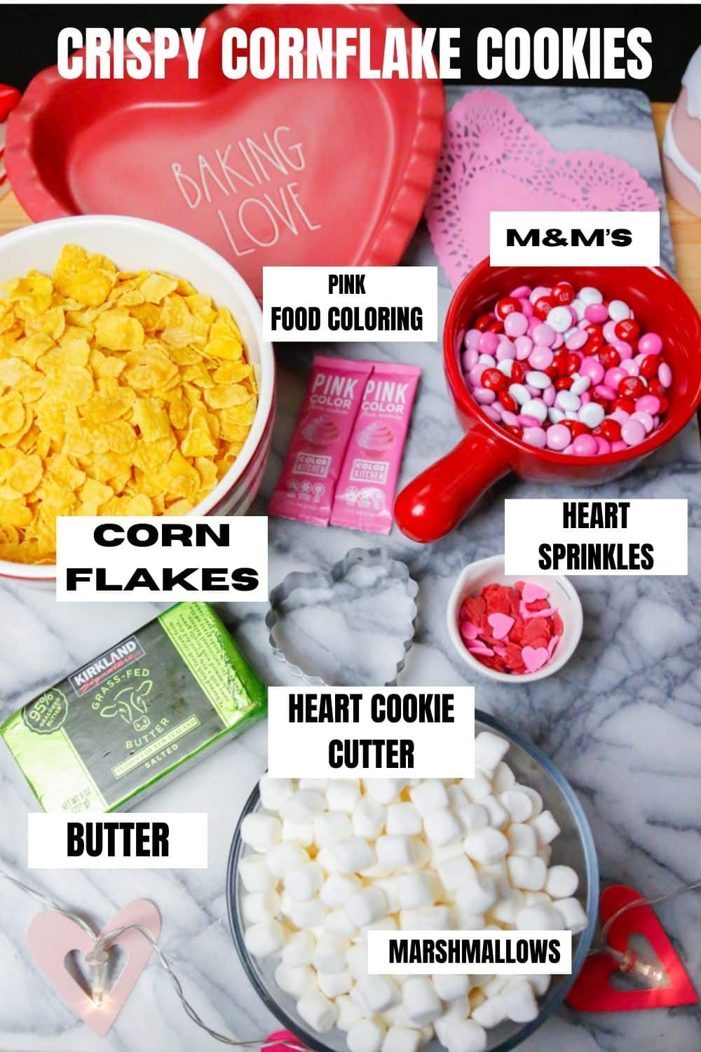 ingredients for crispy cornflake cookies including mini marshmallows, pink food coloring, cornflakes, m&m's, heart sprinkles, butter, heart shaped cookie cutter 