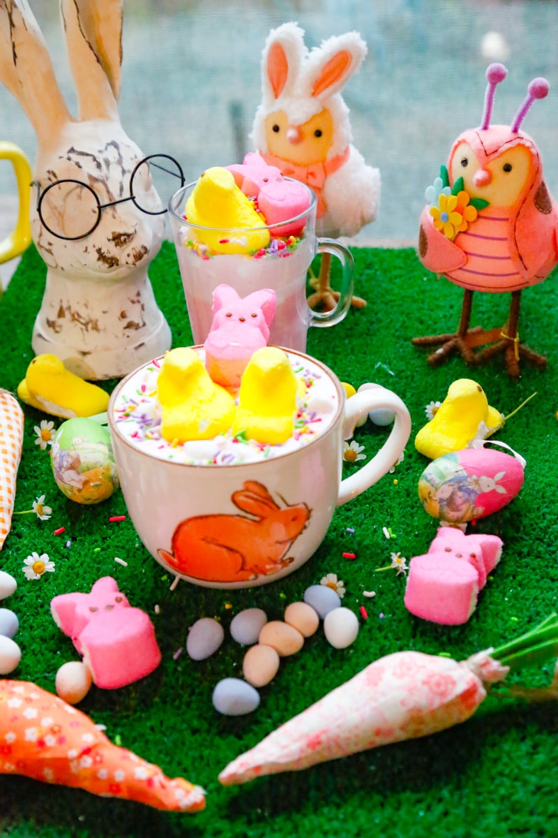 Easter peeps hot chocolate with fabric carrots, mini chocolate eggs, a bunny statue with glasses and easter birds with pink bunny peeps 