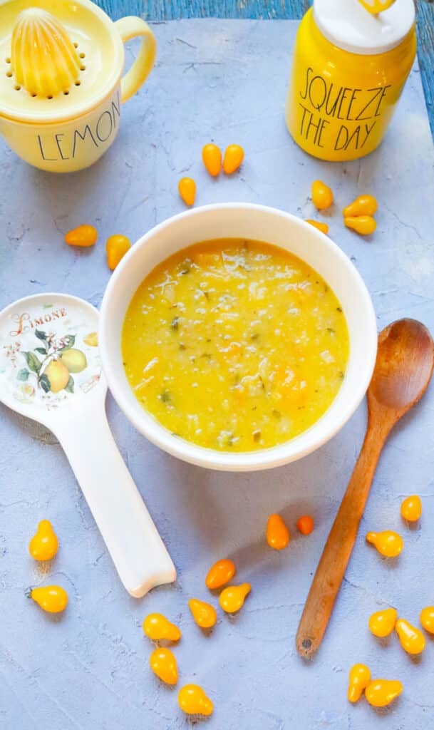 yellow tomato sauce in a mixing bowl on a blue backdrop with mini lemon pear tomatoes, wooden spoon, lemon mixer, squeeze the day canister on a blue backdrop
