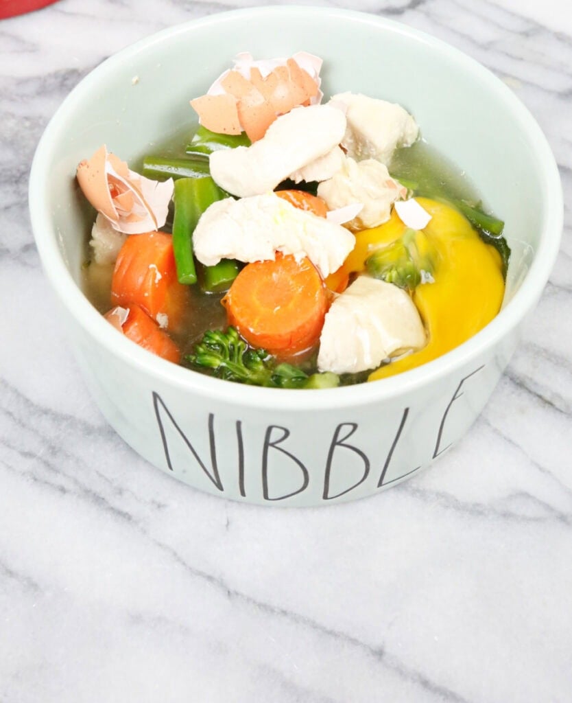 a bowl with the word nibble and filled with homemade dog food, chicken, carrots, broccoli, and eggs and bone broth