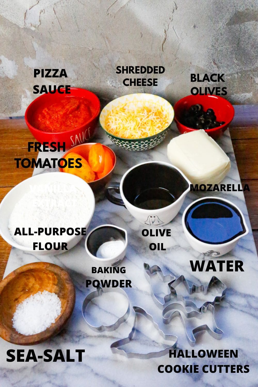 Ingredients for spooky pizza include black olives, water, sea-salt, all-purpose flour, baking powder, fresh tomato slices, Halloween cookie cutters, pizza sauce, shredded cheese, olive oil, fresh mozzarella