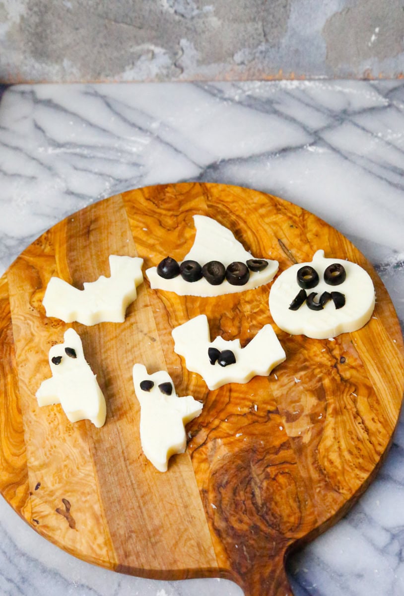 To make the Mozzarella ghosts and Halloween cheese shapes, slice the mozzarella into even slices and place a cookie cuter shape into each slice. Cut the black olives in half and use these for the eyes and ghost face. You can use the black olive to decorate the bats, jack-o-lantern, and witch hats too.