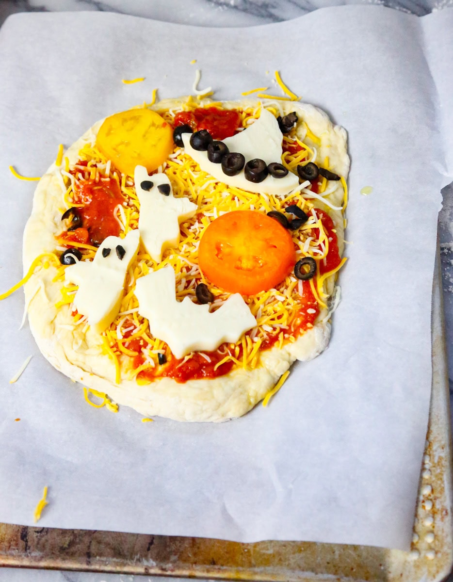 Let's make our pizza! Spread the marinara or pizza sauce of choice lightly on your prepare pizza crust. Top with shredded cheese and tomato slices. Add your Halloween mozzarella shapes where you want on your pizza. Decorate your pizza to your hearts content with your favorite toppings, but make sure the halloween shapes, ghosts, bats, witch hat, and jack-o-lantern are the stars of the show. This is a Halloween pizza after-all!