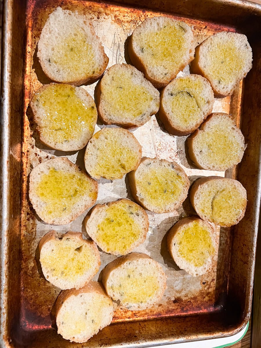 Slice the sourdough baguette and place on a baking sheet. Brush each slice with Extra Virgin Olive Oil and rub with a clove of garlic. This brings out the most flavor! 