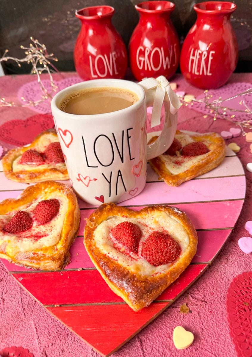 Heart shaped strawberry cream cheese danish with coffee in a “Love Ya” mug on a pink Valentine’s Day background