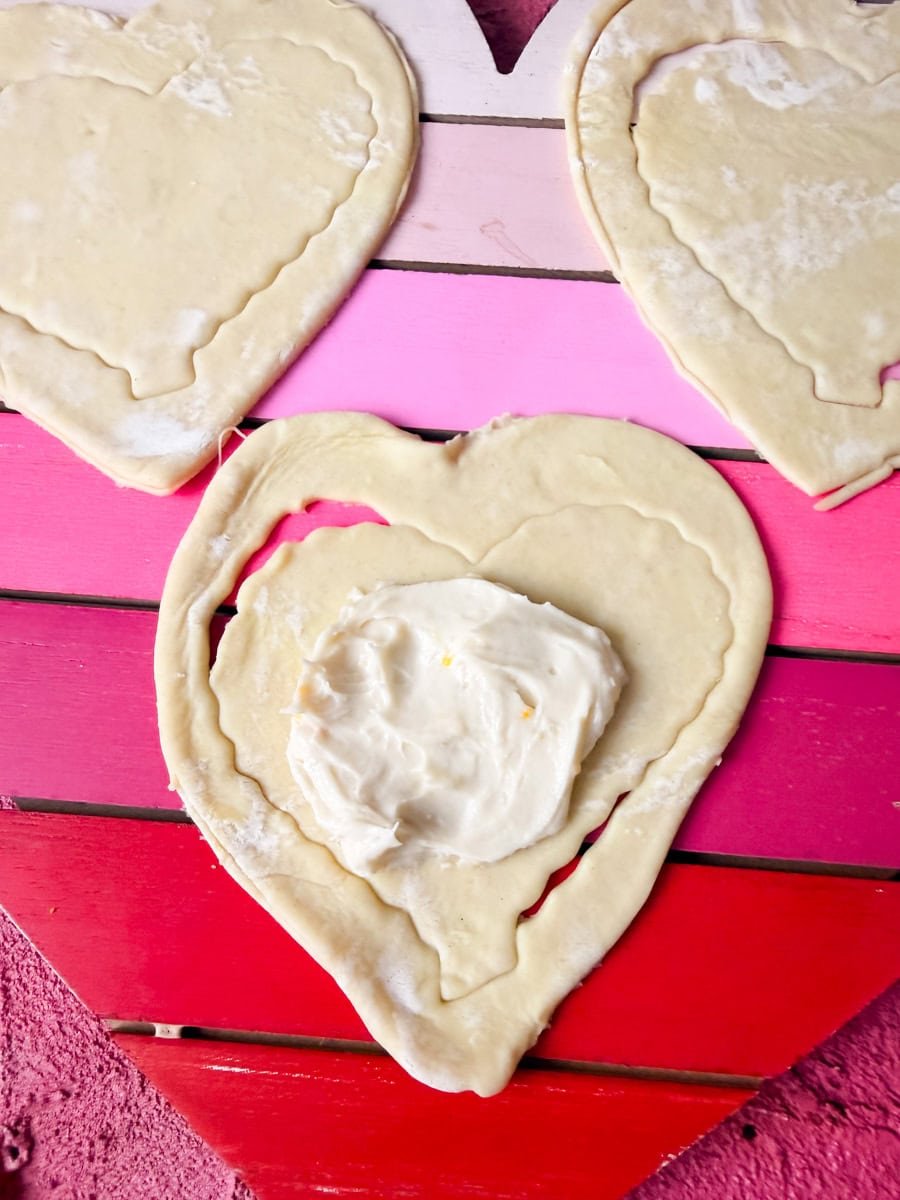 Heart-shaped puff pastry with cream cheese filling being added to center before baking 