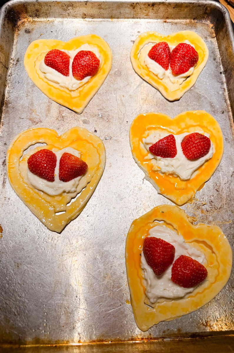 Heart shaped strawberry cream cheese danish made with puff pastry and fresh strawberries on a pink Valentine’s background