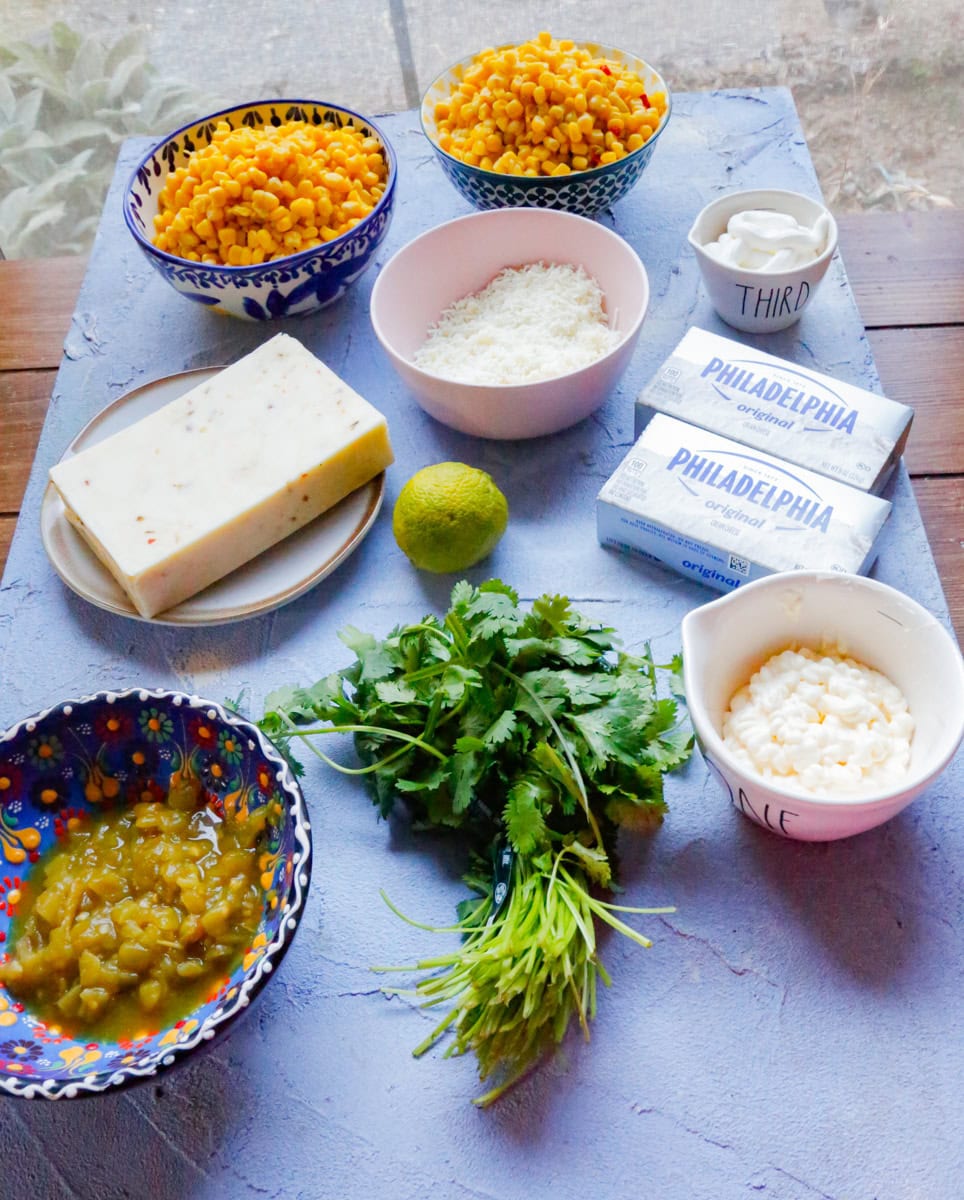 Ingredients for slow cooker Mexican street corn dip recipe including corn, cream cheese, Monterey Jack, cotija cheese, sour cream, mayonnaise, lime, cilantro, and diced green chiles.