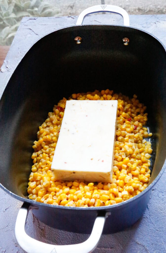  Block of Pepper Jack cheese placed on top of corn in slow cooker for elote corn dip