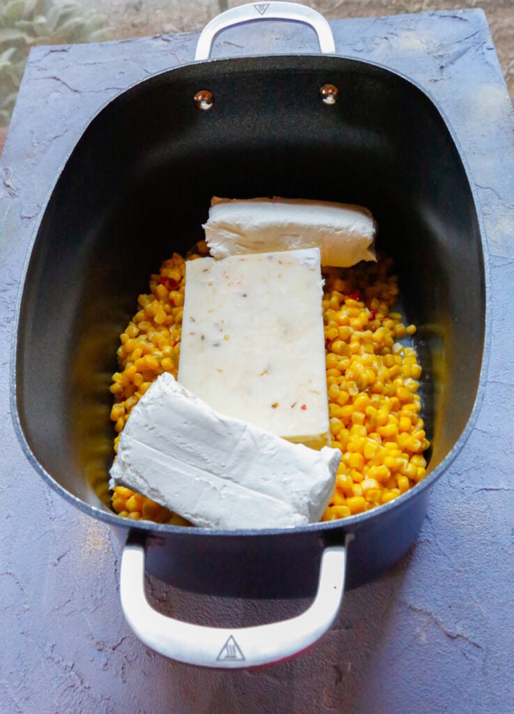Cream cheese blocks and pepper jack cheese added over corn in a slow cooker for Mexican street corn dip