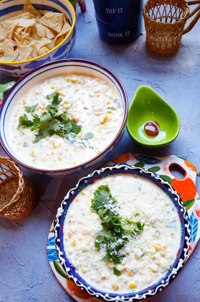 Slow cooker Mexican street corn dip garnished with fresh cilantro and cotija cheese, served warm with tortilla chips