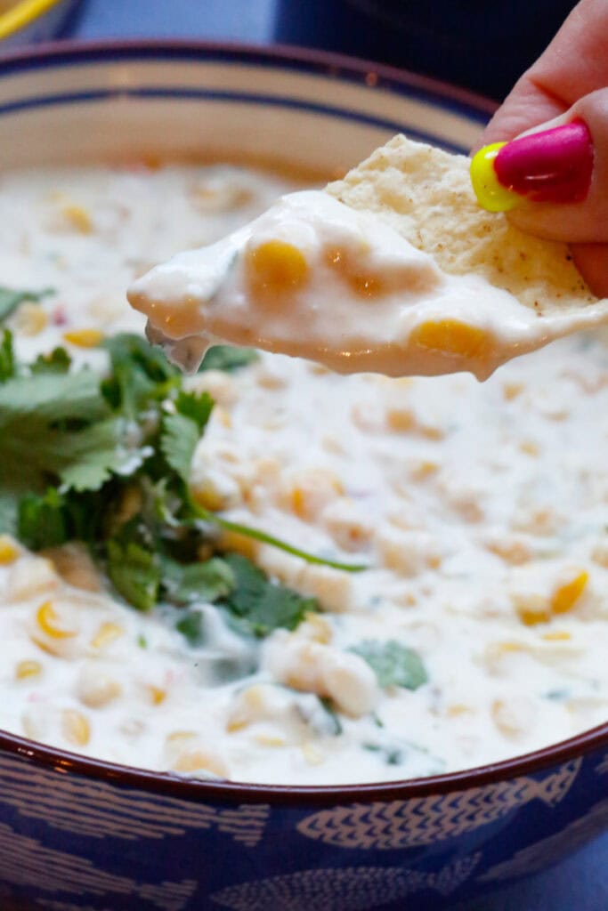 
Tortilla chip dipped into creamy slow cooker Mexican street corn dip with corn kernels, cream cheese, Cotija, and fresh cilantro
