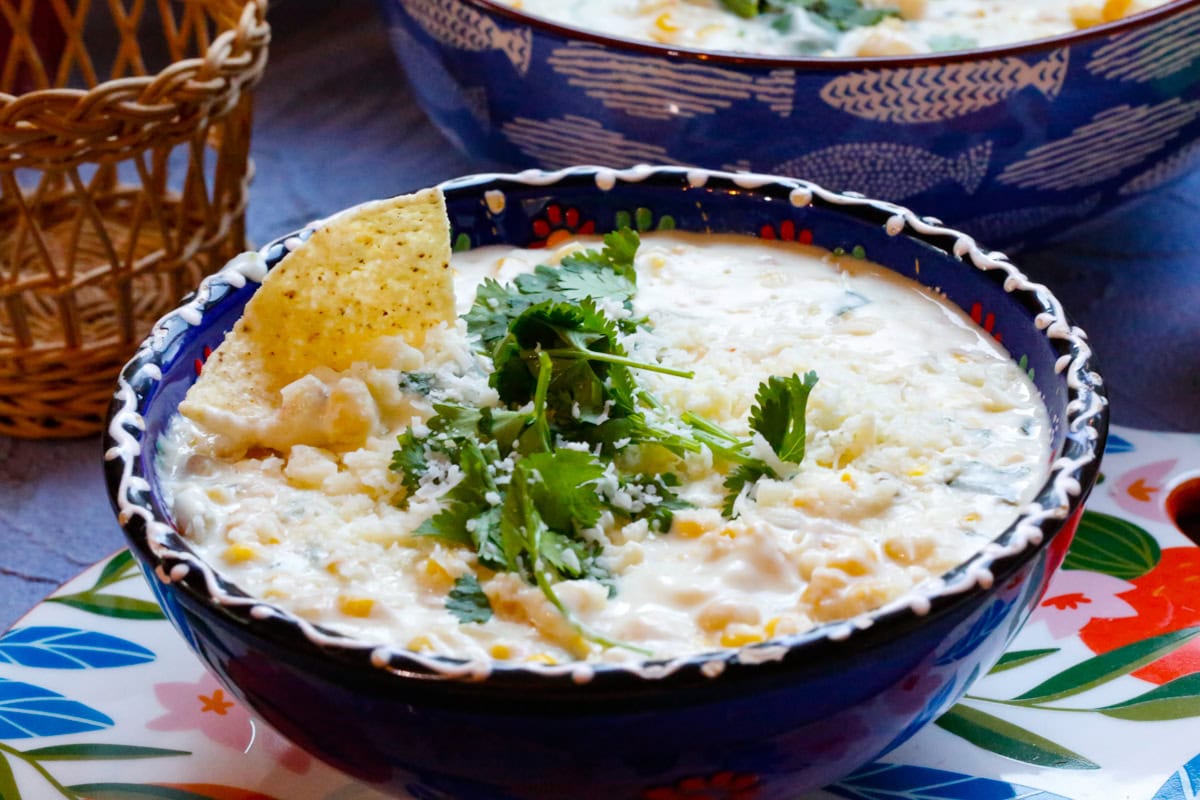 
Close-up of creamy Mexican street corn dip with cream cheese topped with cilantro and cotija cheese served in a bowl with tortilla chips