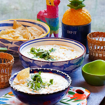 Easy slow cooker Mexican street corn dip recipe served in bowls with cilantro garnish, tortilla chips, and a festive party table setup.