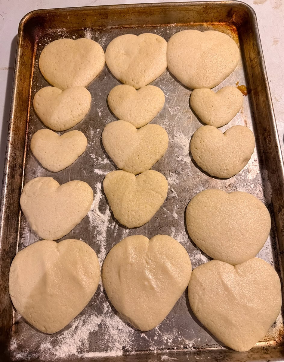 Baked heart shaped sugar cookies on a parchment lined baking sheet, ready to decorate for Valentine’s Day conversation hearts cookies