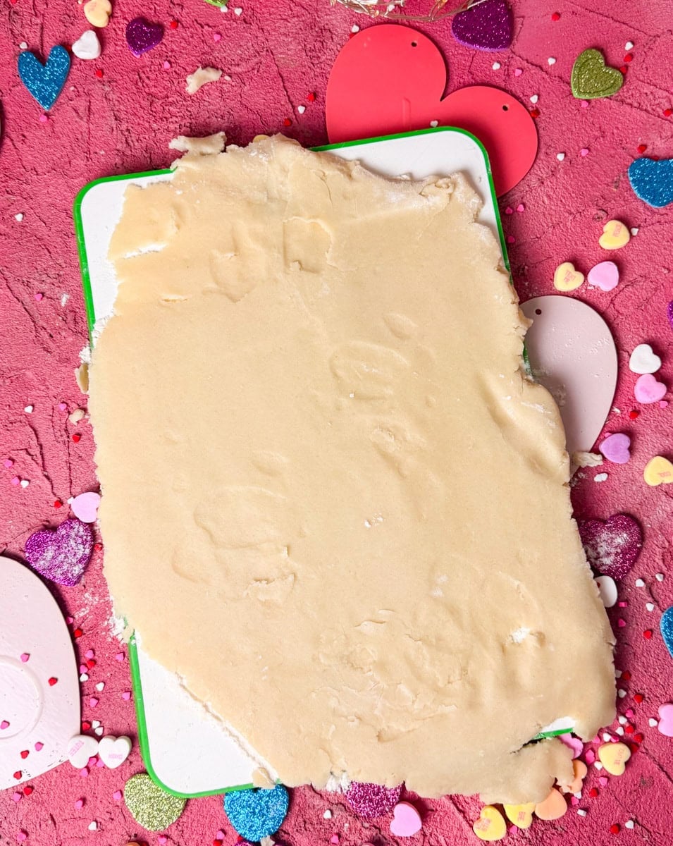 Rolled sugar cookie dough on parchment paper before cutting heart shaped cookies for Valentine’s Day conversation hearts cookies