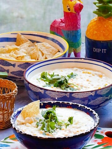 Creamy slow cooker Mexican street corn dip topped with fresh cilantro, served in blue bowls with tortilla chips for dipping
