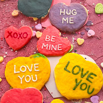 Frosted conversation heart sugar cookies with royal icing sayings including “XOXO,” “HUG ME,” and “BE MINE,” styled for a Valentine’s Day cookie recipe.
