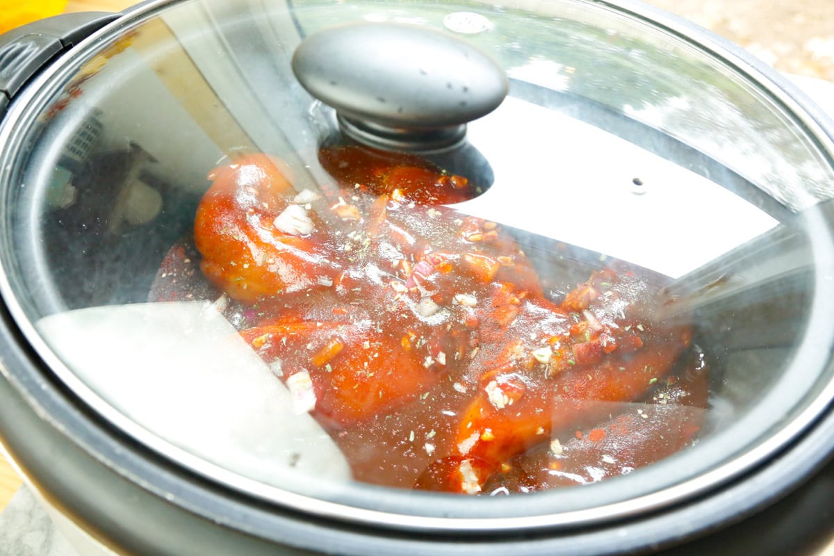 BBQ sauce, onions, and seasonings poured over chicken breasts in a slow cooker for shredded barbecue chicken sandwiches