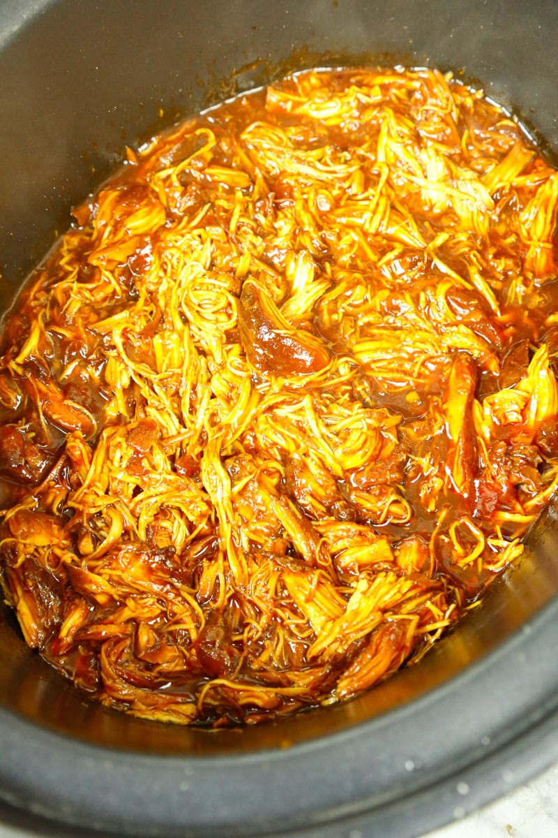 Shredded BBQ pulled chicken in a slow cooker coated in rich barbecue sauce, ready for sandwiches