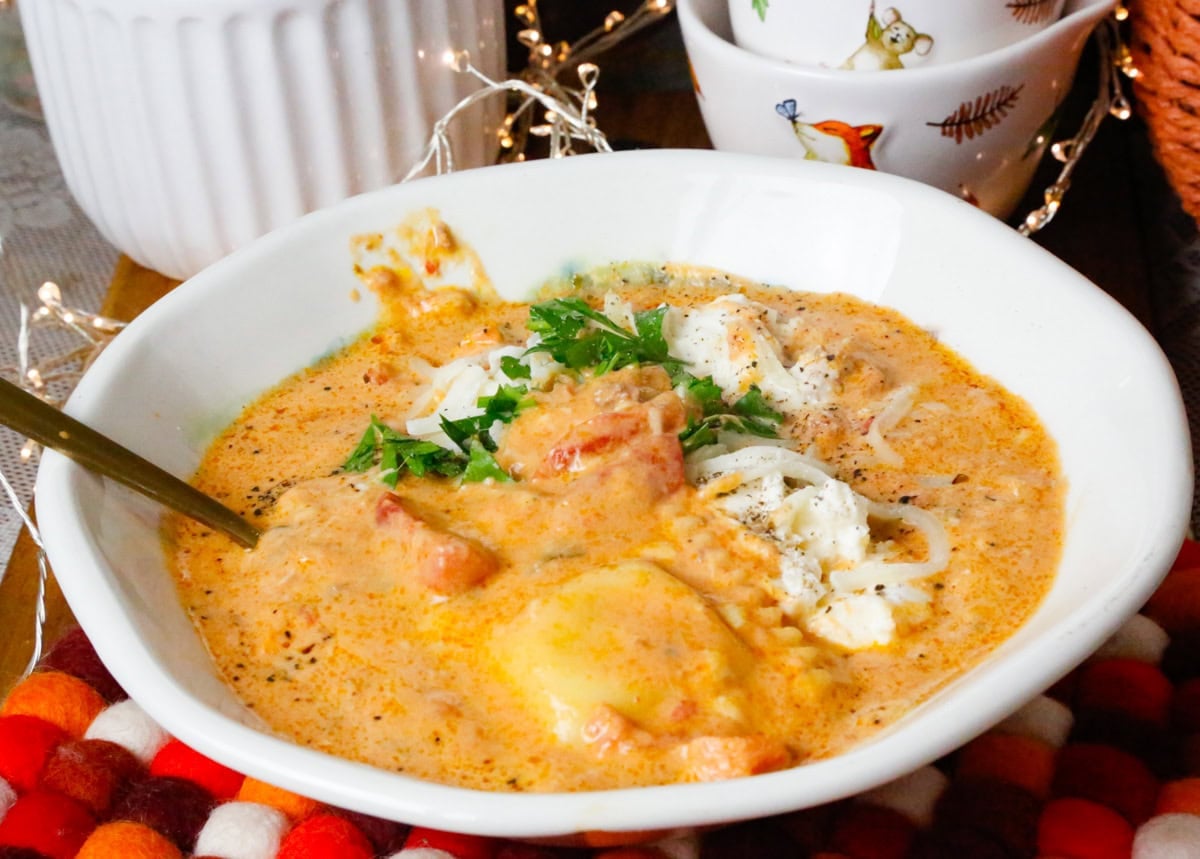 Creamy slow cooker ravioli soup served in a white bowl topped with ricotta and fresh parsley