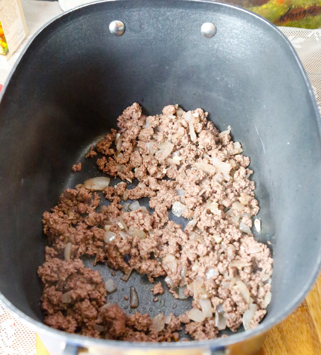 Ground beef and diced onions browning in a pot for slow cooker ravioli soup recipe