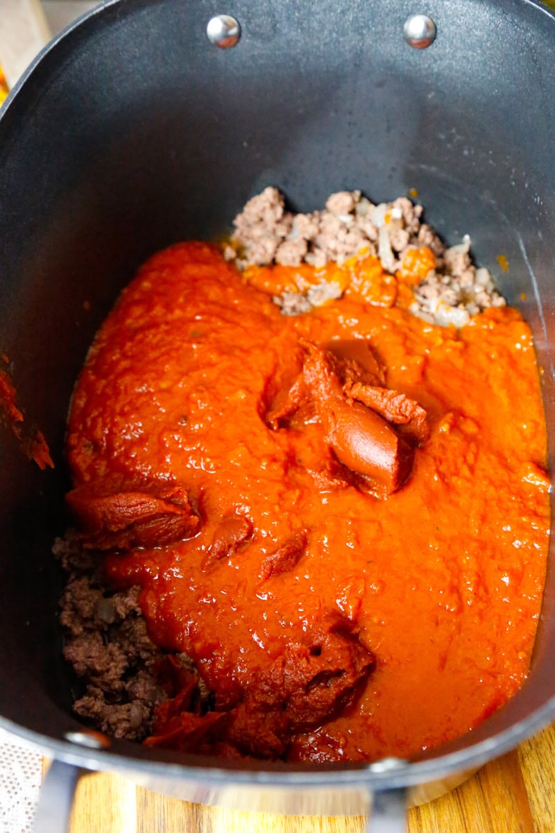 Tomato sauce and browned ground beef layered in slow cooker for ravioli soup