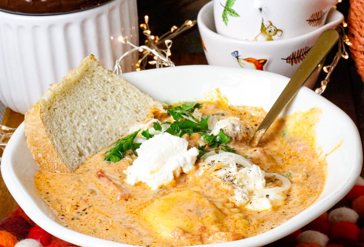 Slow cooker ravioli soup with ground beef, spinach, and cheese ravioli in a creamy tomato broth served with bread.