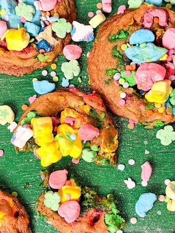 Soft baked Lucky Charms cookies topped with colorful cereal marshmallow pieces and sprinkles on a green background