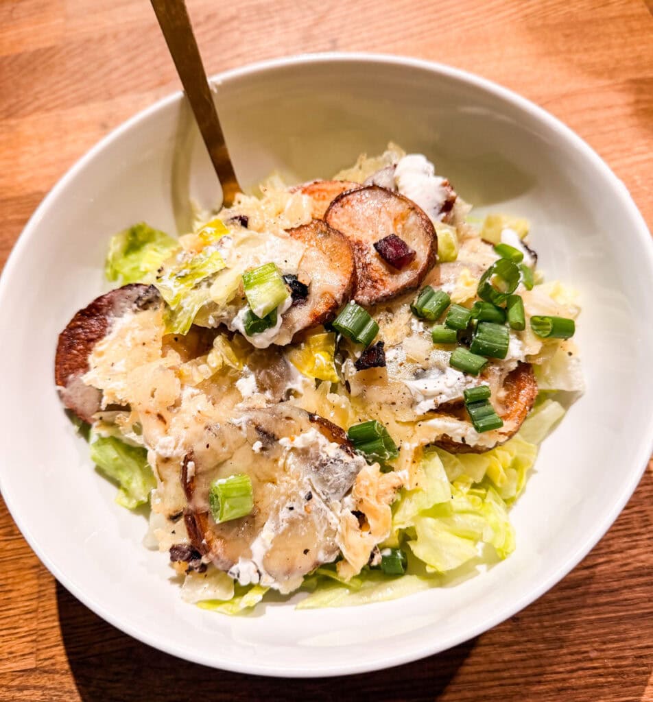 Bowl of Irish nachos made with crispy roasted potato slices, melted cheddar cheese, bacon, sour cream, lettuce, and green onions
