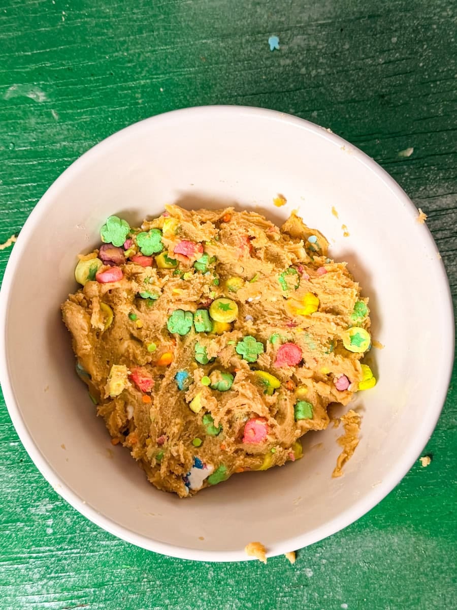 Cookie dough mixed with colorful Lucky Charms marshmallows and sprinkles in a bowl