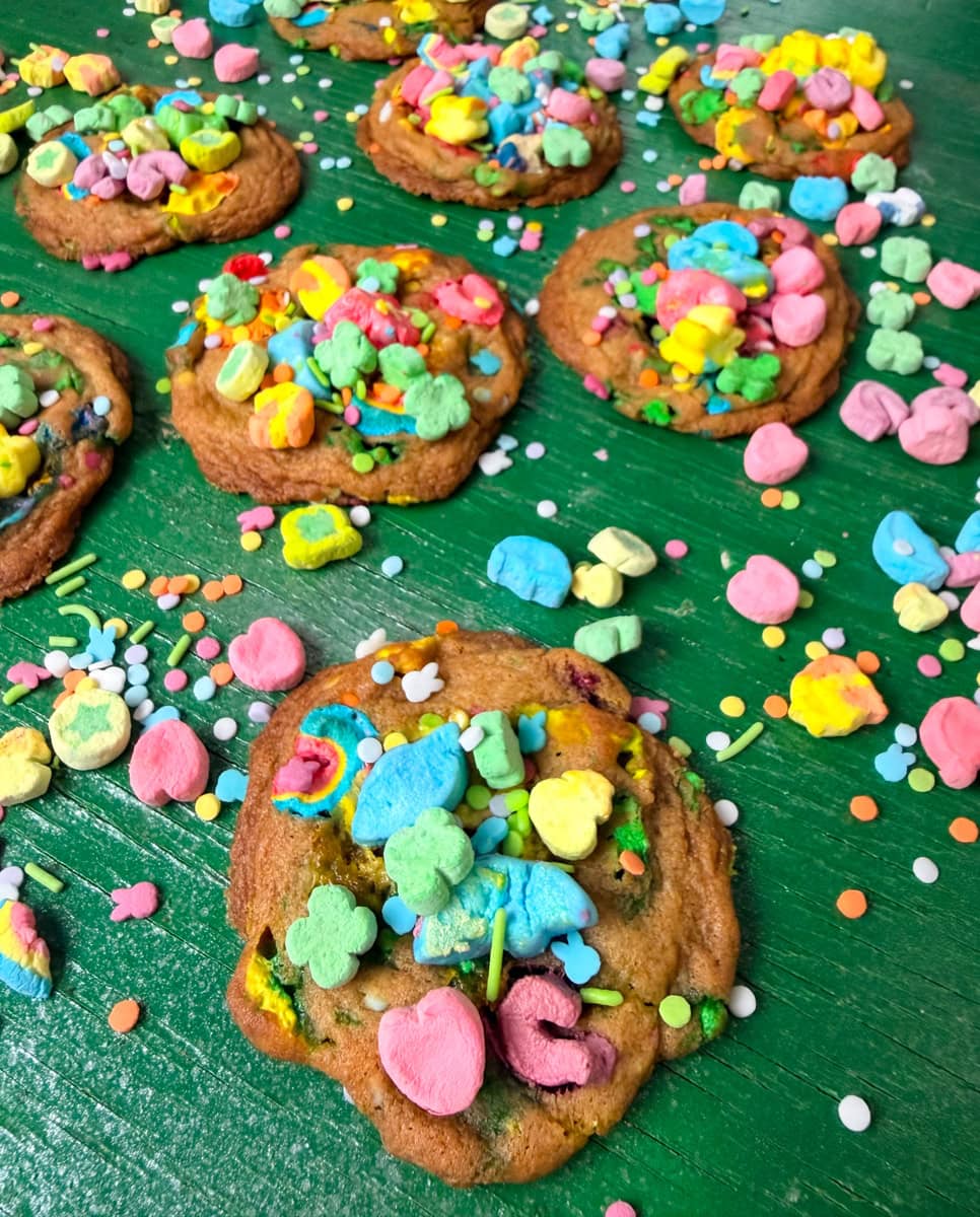 Close-up of soft baked Lucky Charms cookies topped with colorful cereal marshmallows and sprinkles on a green surface