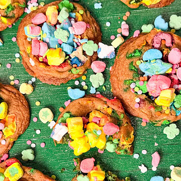 Soft baked Lucky Charms cookies topped with colorful marshmallow cereal pieces and sprinkles on a green background