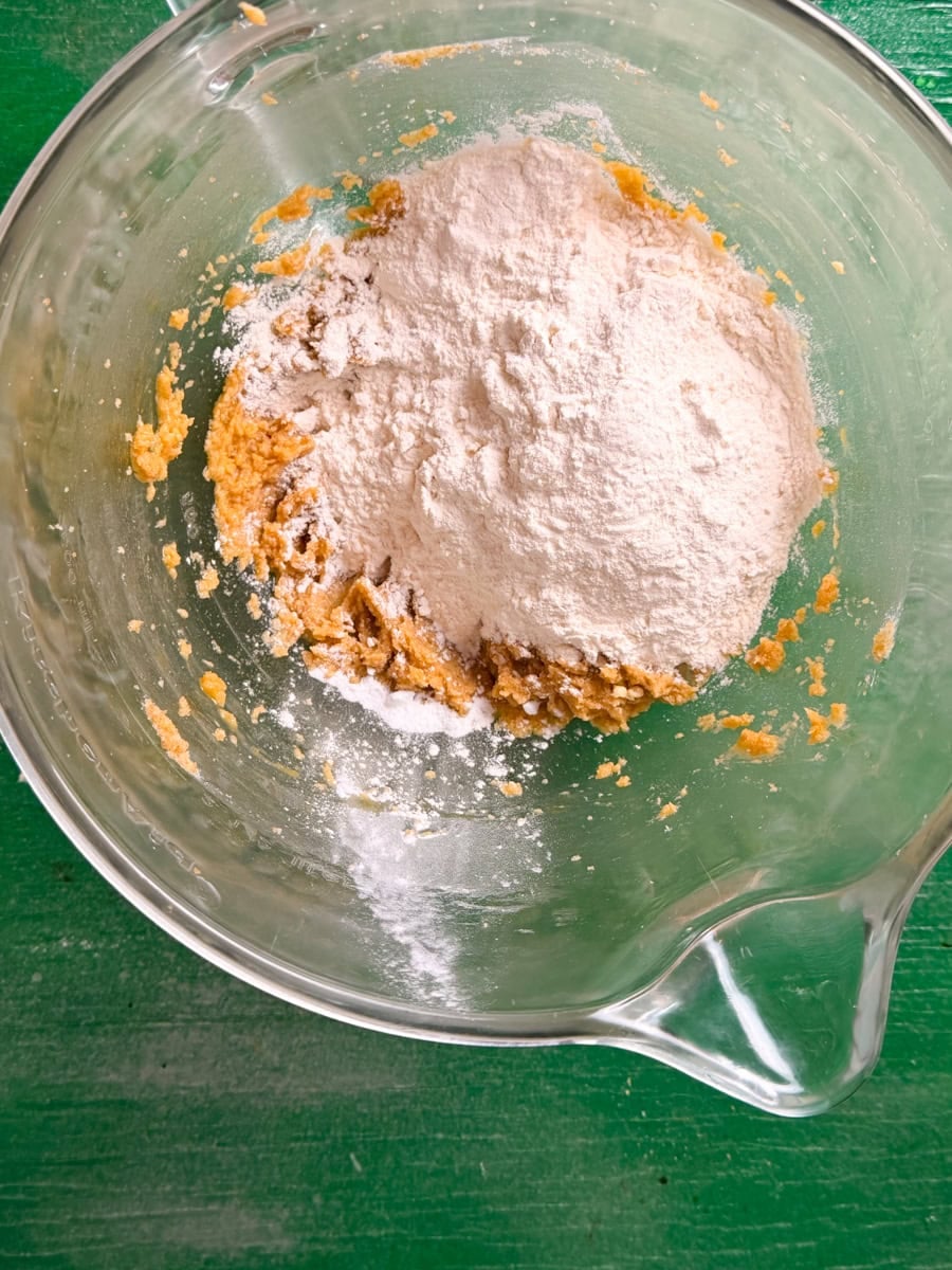 Flour, baking soda, and salt being added to a bowl of creamed butter and sugar