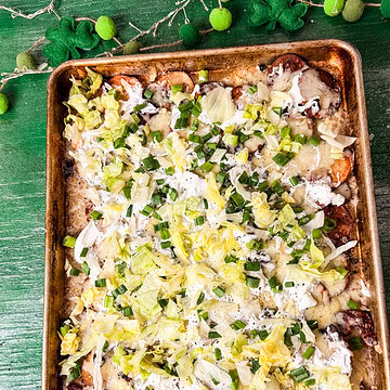 Sheet pan Irish nachos made with crispy roasted potato slices, melted cheese, bacon, sour cream, shredded lettuce, and green onions on a festive St. Patrick’s Day background