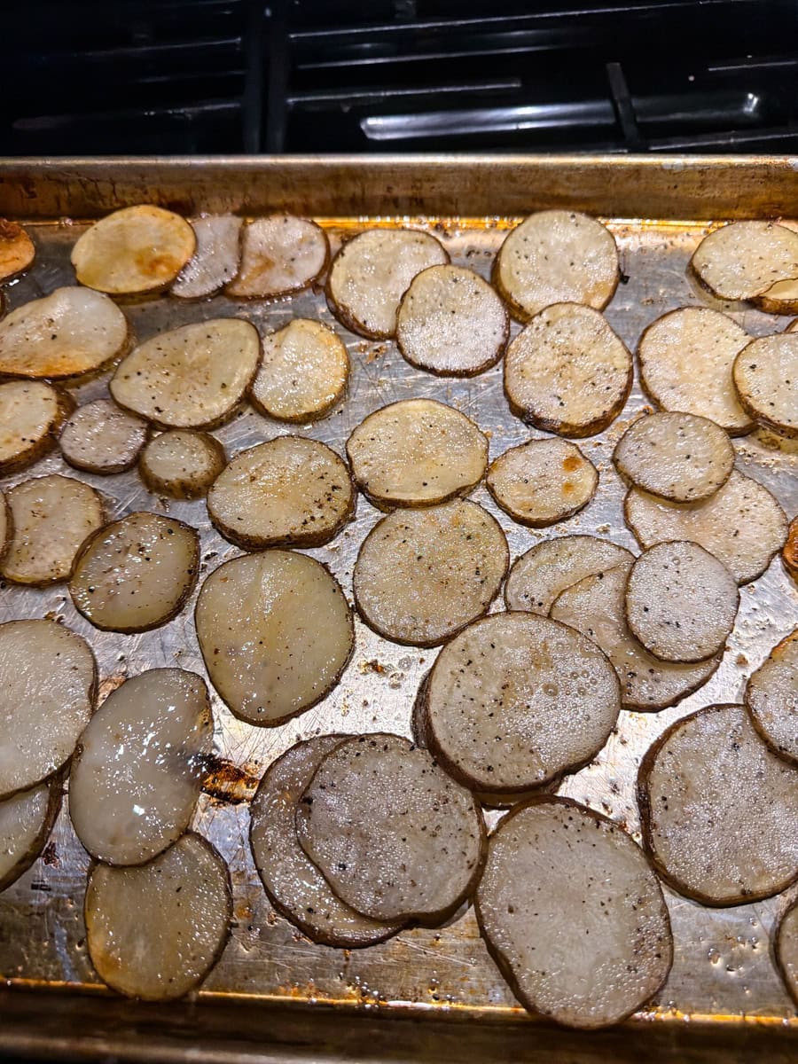 Sliced russet potatoes coated with melted butter, salt, and pepper in a bowl before baking Irish nachos