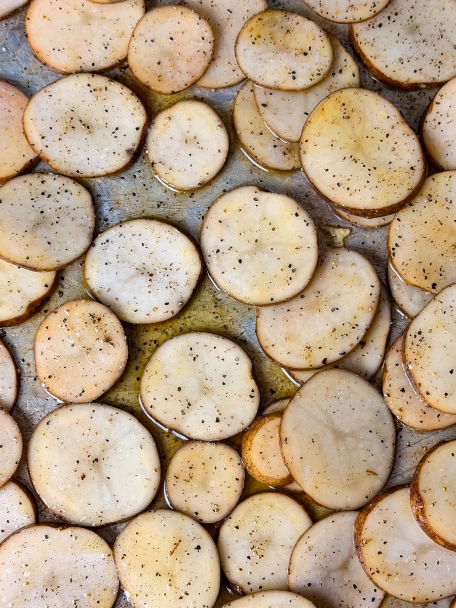 Thinly sliced russet potatoes seasoned with salt and pepper and drizzled with melted butter on a baking sheet for Irish nachos