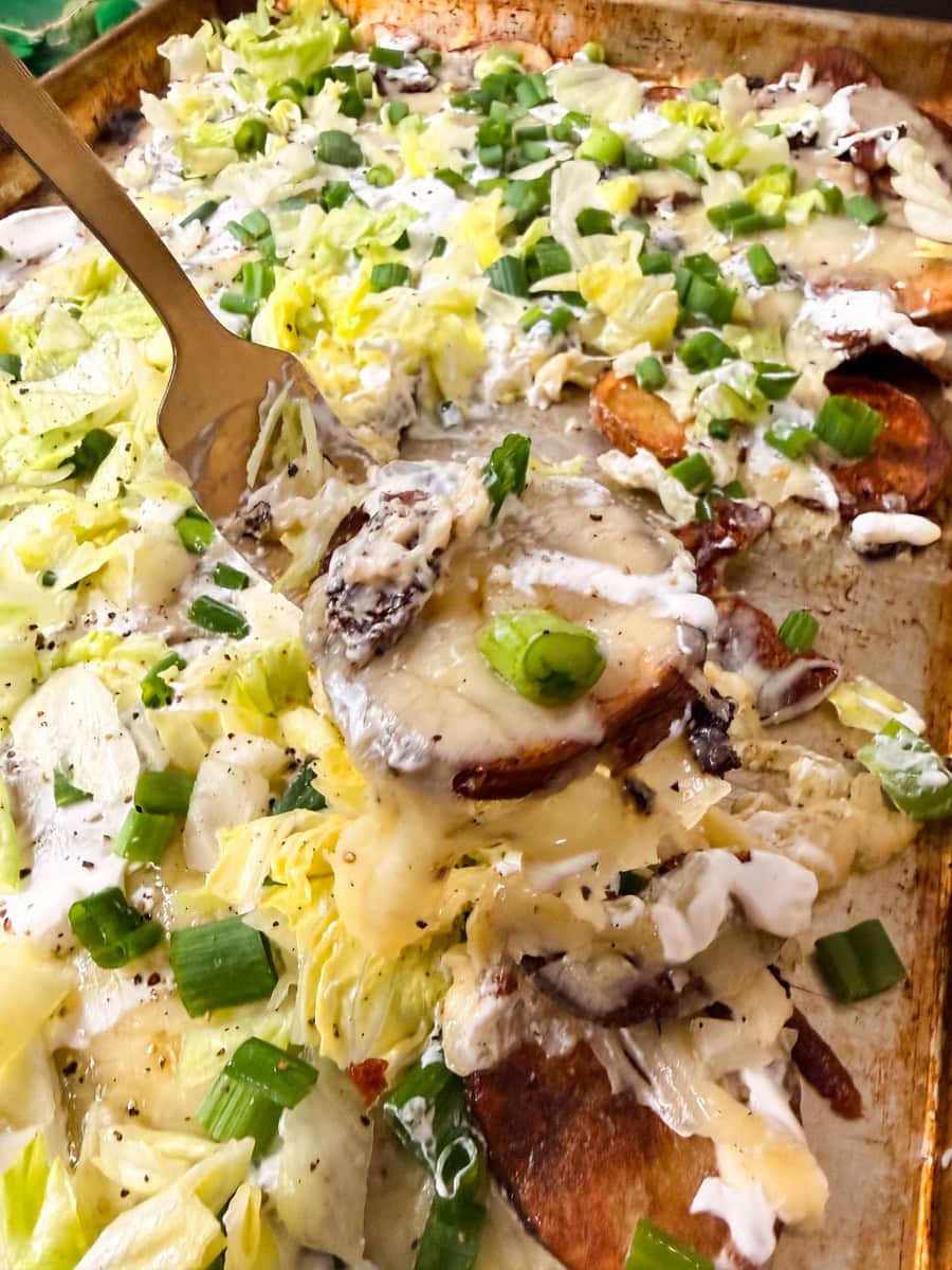 Fork lifting cheesy Irish nachos with crispy potato slices, sour cream, lettuce, and green onions