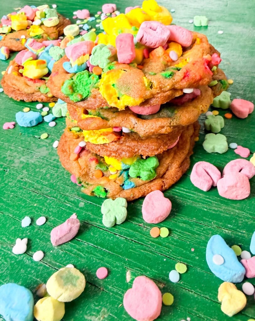 Lucky Charms cookies stacked with colorful marshmallow cereal pieces and pastel sprinkles on a green background