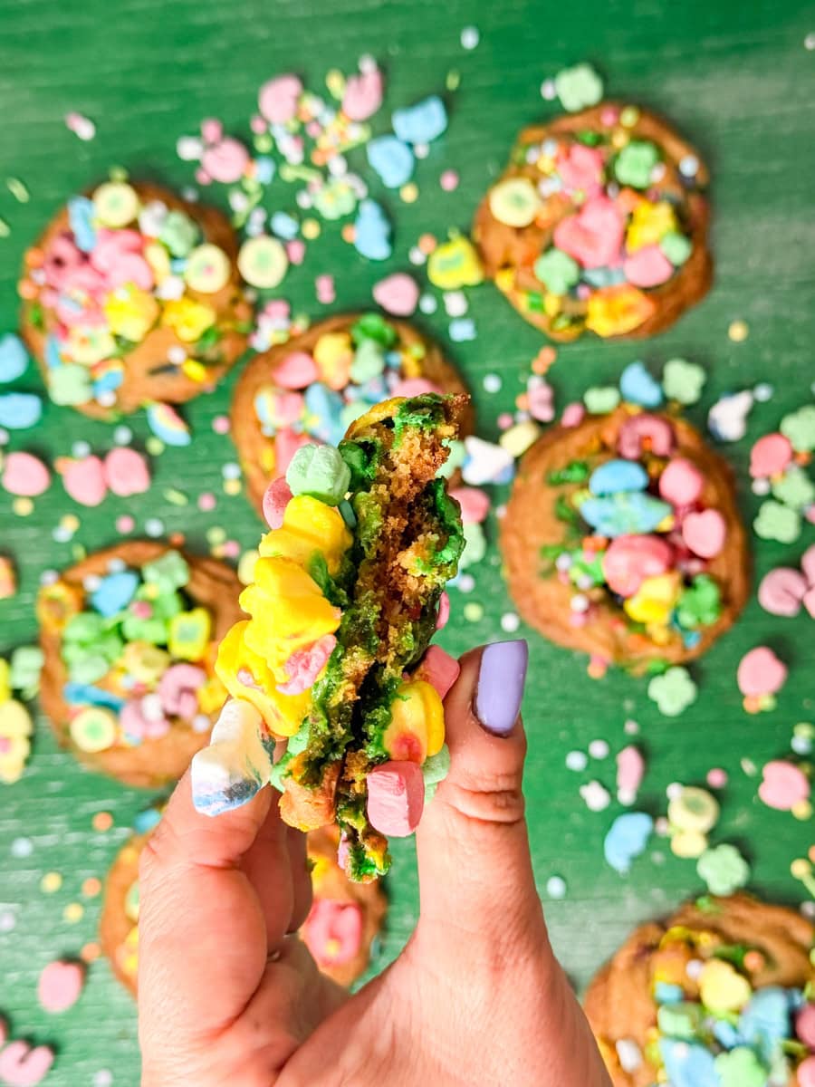 Lucky Charms cookie broken in half showing a soft green center with colorful marshmallow cereal pieces.