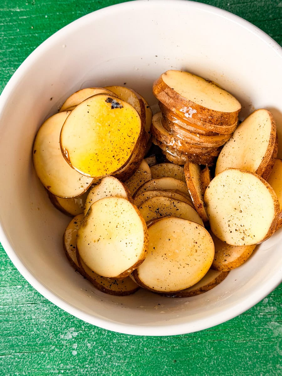 Sliced russet potatoes coated with melted butter, salt, and pepper in a bowl before baking Irish nachos