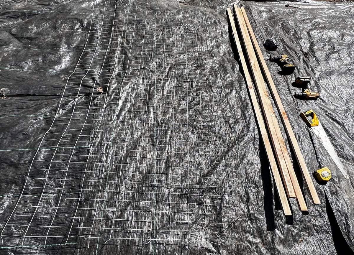 
materials for wooden garden trellis including hog wire panel and 1x3 wood boards laid out before building