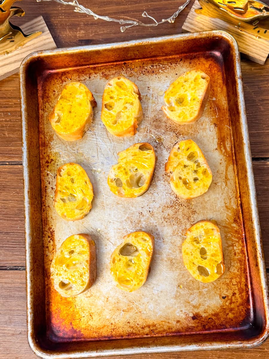 toasting baguette slices with olive oil on baking sheet for crostini appetizer
