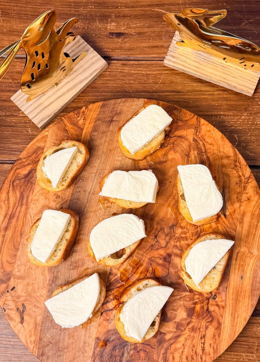 adding fresh mozzarella slices to toasted baguette for ladybug crostini appetizer