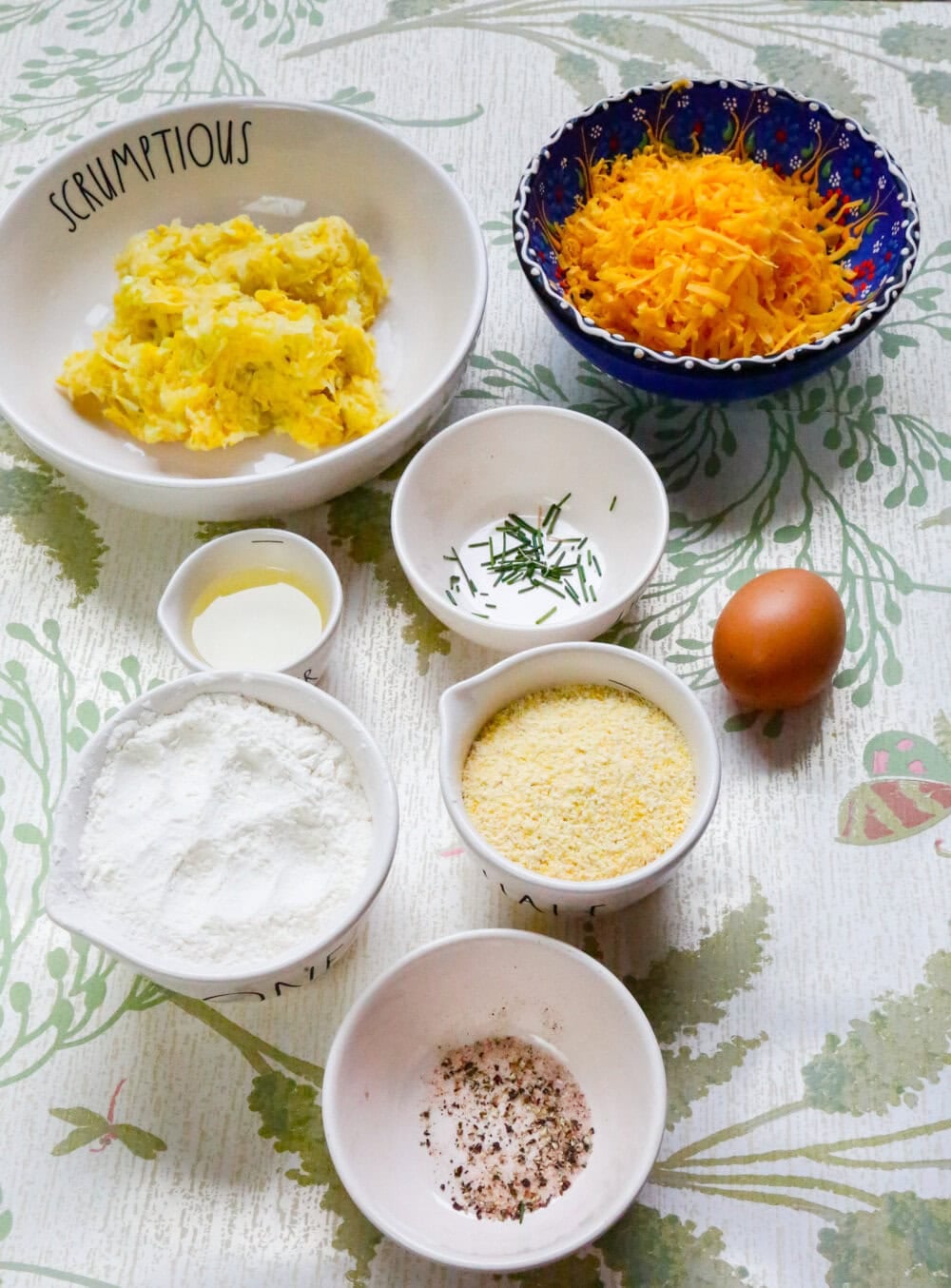 Yellow squash fritter ingredients arranged on a table including grated squash, flour, cornmeal, egg, fresh chives, cream, salt, and pepper.