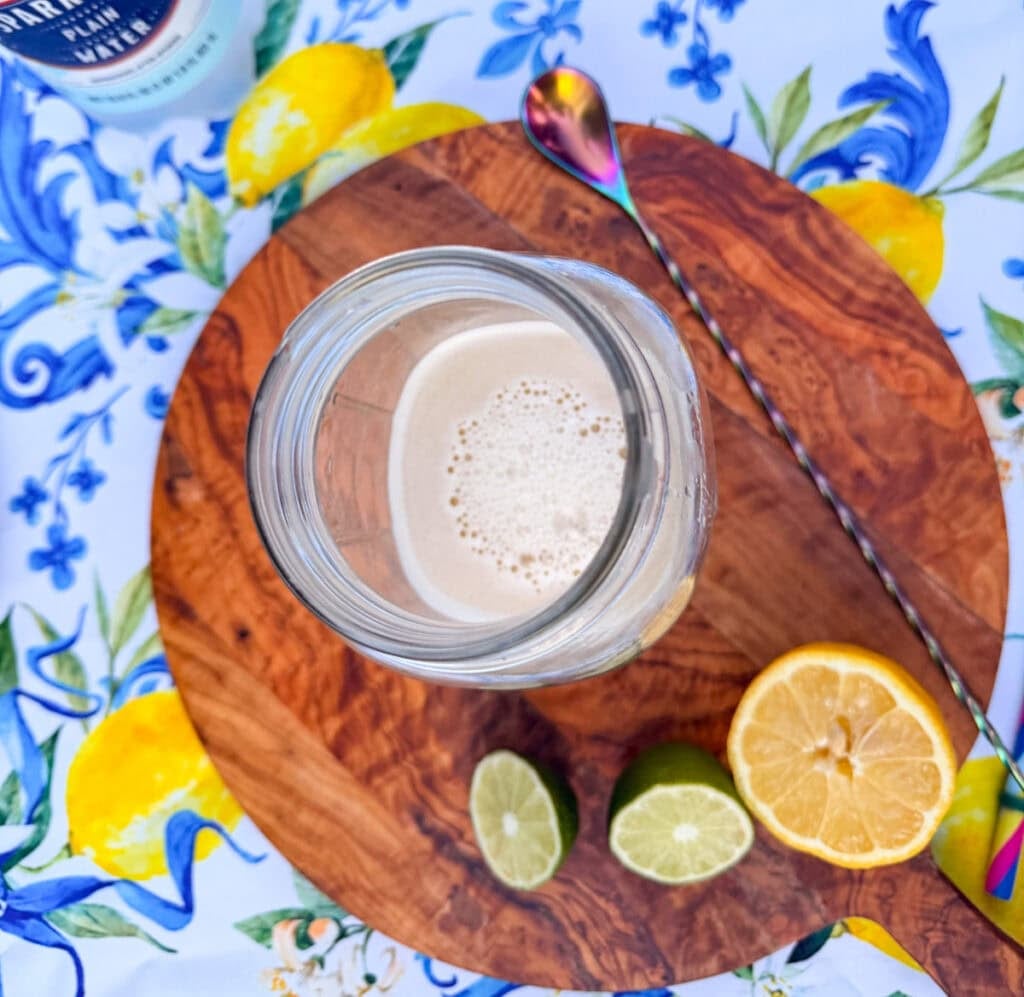 Step two for healthy homemade lemon lime soda recipe showing fresh lemon and lime juice added to maple syrup and Baja sea salt in a mason jar before mixing.